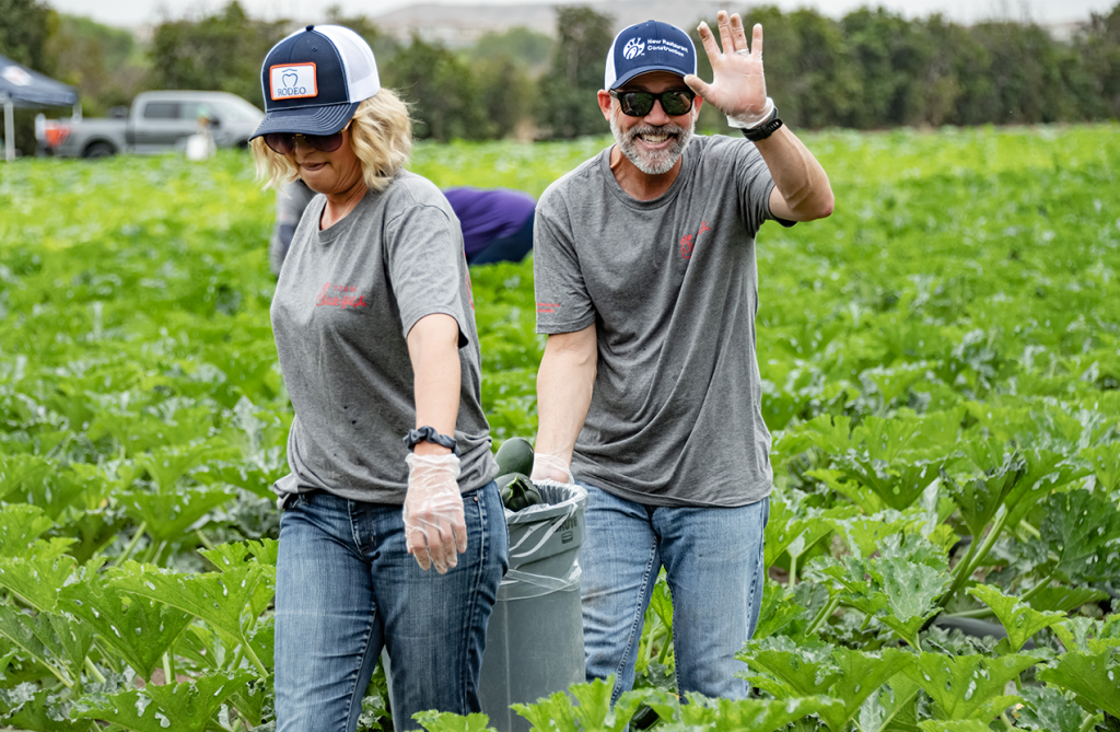 Two people walking through a garden and carrying a large bucket