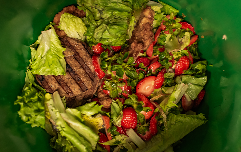 A container with scraps lettuce, strawberry slices, meat
