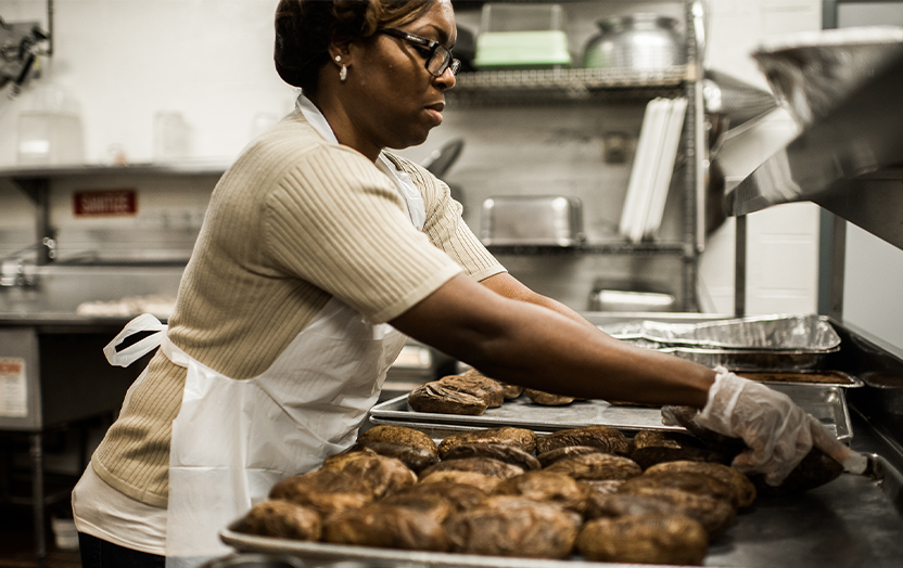 A person placing baked potatoes on a pan