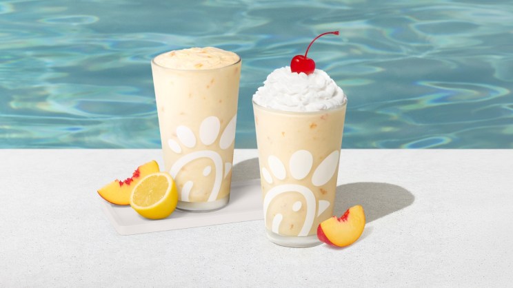Two glasses of Chick-fil-A's Peach Milkshake and Peach Frosted Lemonade sitting by a pool.