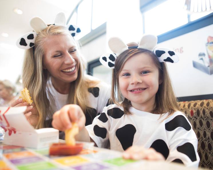 Chick-fil-A Guests dressed up as cows sitting at a table eating Waffle Fries.