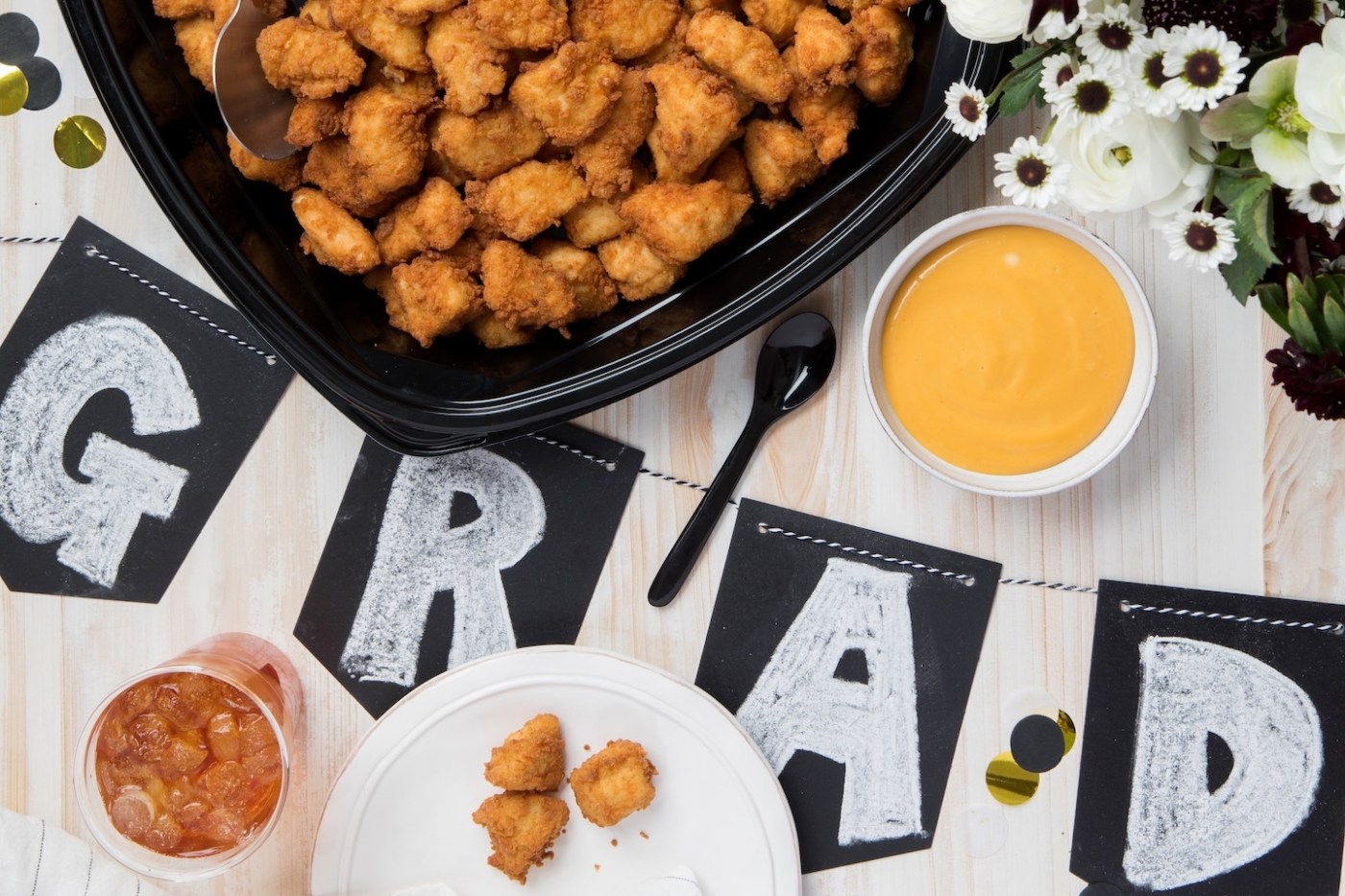 Chick-fil-A® Nugget Tray on a table with flowers, plates of Chick-fil-A® Nuggets and a “Grad” sign