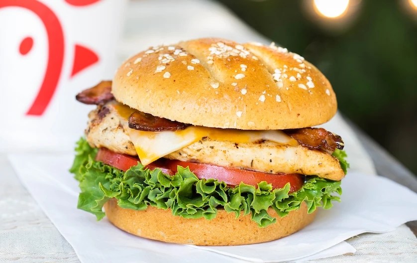 Chick-fil-A® Grilled Chicken Club Sandwich on white napkins on a table with lights and a beverage in the background