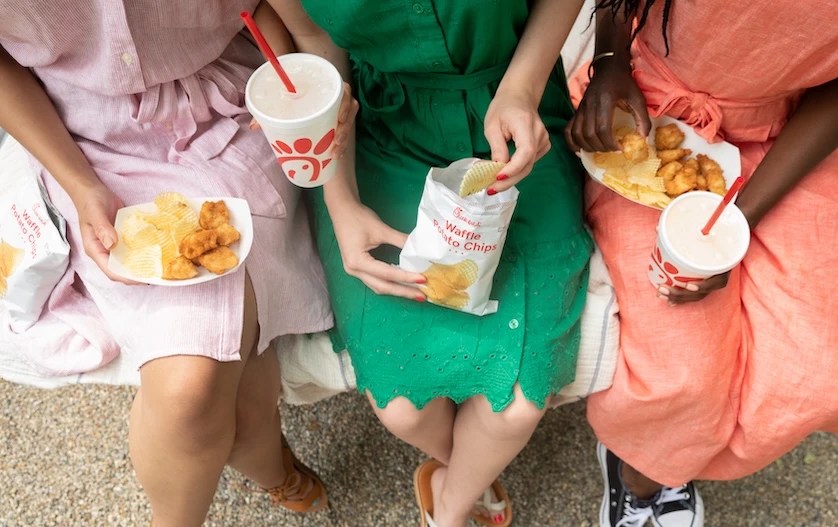 Three people sitting together with plates of Chick-fil-A® Nuggets and Waffle Potato Chips with beverages.