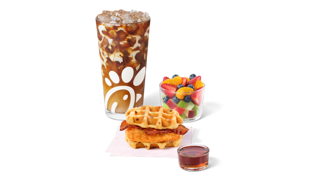Chicken & Waffles Breakfast Sandwich on napkins with a side of Classic Syrup next to a Cream Cold Brew and a Fruit Cup