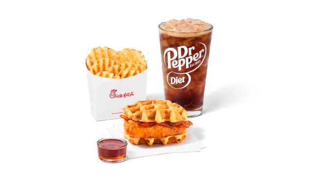 Chicken & Waffles Sandwich on napkins with a side of Classic Syrup next to Waffle Fries and a Diet Dr Pepper