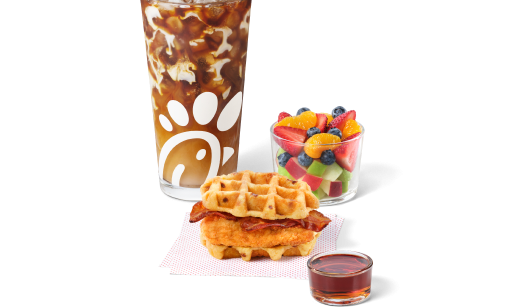 Chicken & Waffles Breakfast Sandwich on napkins with a side of Classic Syrup next to a Cream Cold Brew and a Fruit Cup