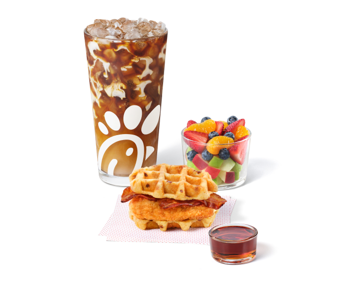 Chicken & Waffles Breakfast Sandwich on napkins with a side of Classic Syrup next to a Cream Cold Brew and a Fruit Cup