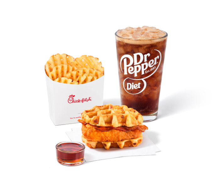 Chicken & Waffles Sandwich on napkins with a side of Classic Syrup next to Waffle Fries and a Diet Dr Pepper