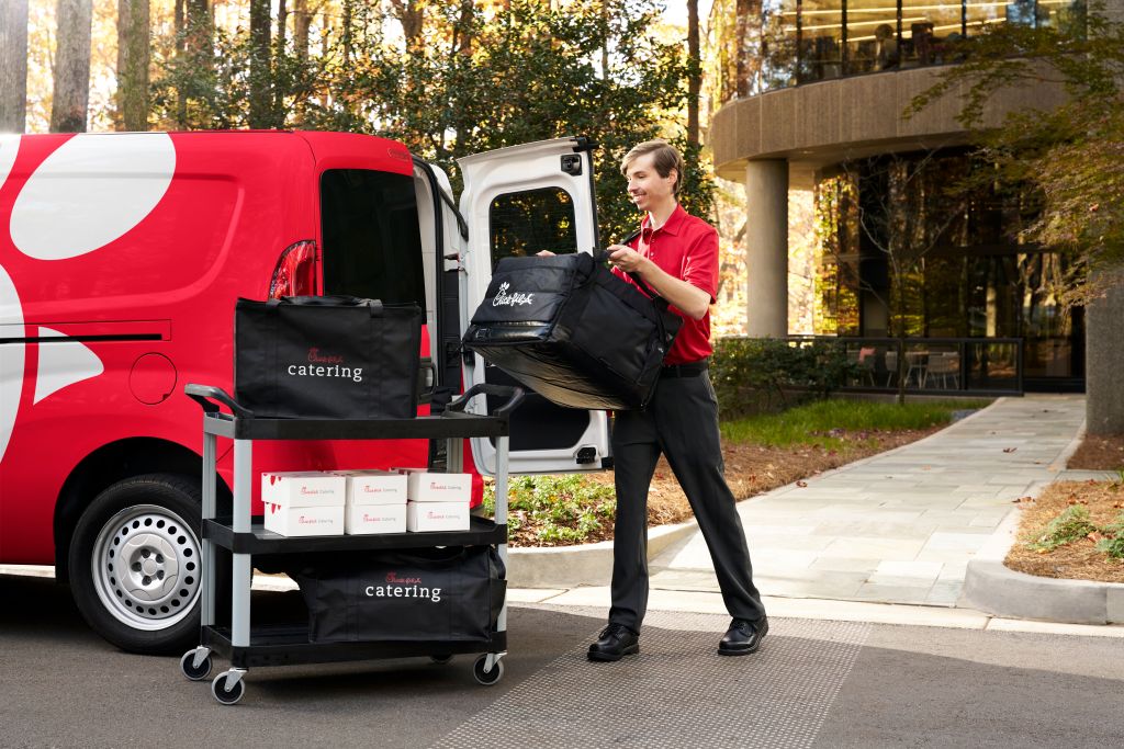 Team Member standing in front of a Chick-fil-A® Delivery truck, placing Chick-fil-A® Catering bags onto a cart