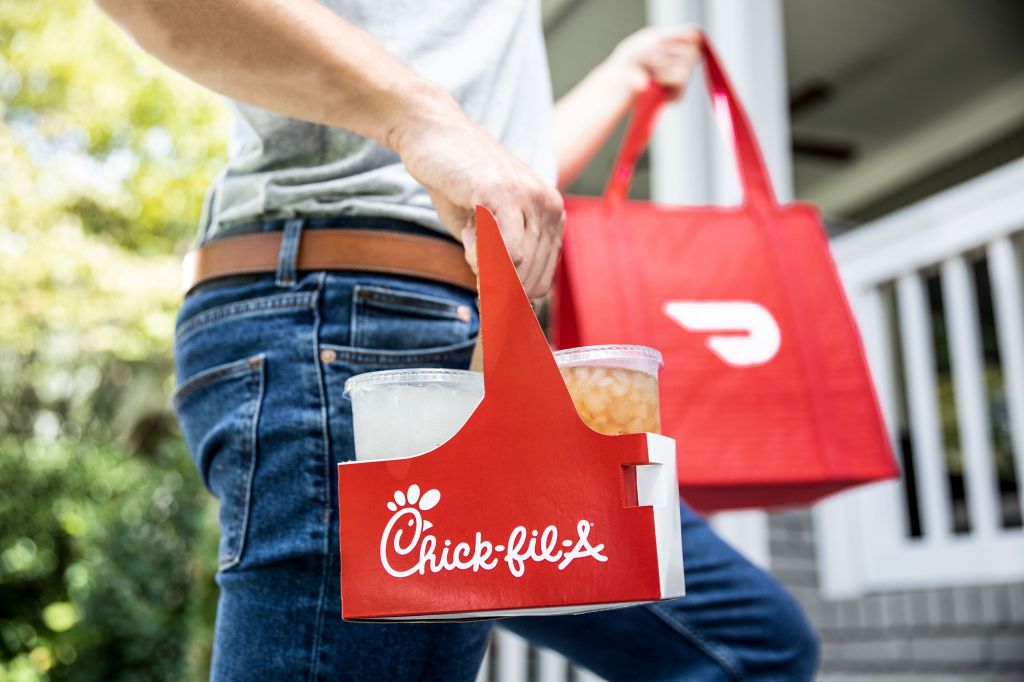 Person holding a DoorDash bag in one hand and a drink carrier with beverages in it in the other hand