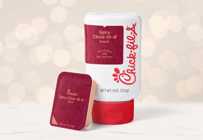 A packet of Spicy Chick-fil-A® Sauce leaning against an 8-ounce bottle of Spicy Chick-fil-A® Sauce